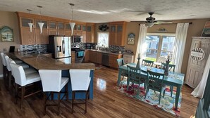 A spacious kitchen with wooden cabinets, a large island with bar stools, a dining area with a table and chairs, and a ceiling fan.
