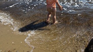 A child walking in shallow water near a dock with a boat and a covered structure.