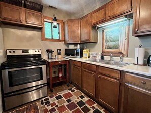 Une cuisine avec des meubles en bois, une cuisinière en acier inoxydable, un four à micro-ondes et une fenêtre donnant sur la forêt.