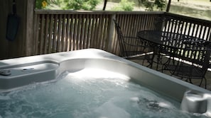 A hot tub with a wooden deck and metal chairs.