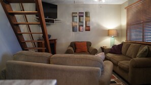 A living room with a sofa set, a wooden ladder, a TV mounted on the wall, and a lamp on a side table.