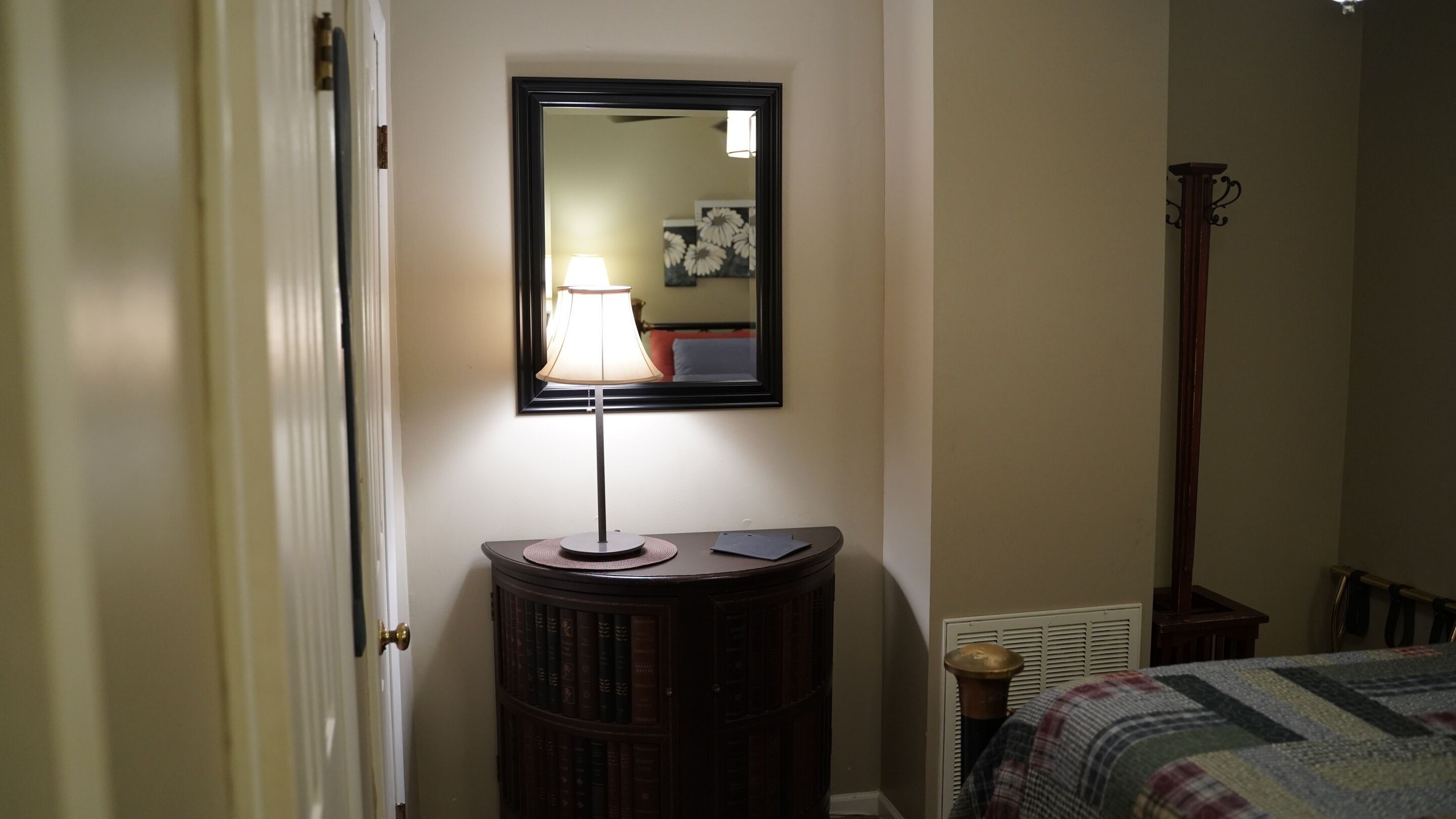 A room with a bedside table, a lamp, a mirror, a radiator, and a bed with a quilt.