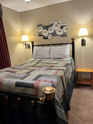A bedroom with a bed, two wall-mounted lamps, a quilt, and a painting of flowers.