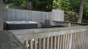 Une terrasse en bois avec un jacuzzi, des chaises en métal et une table.