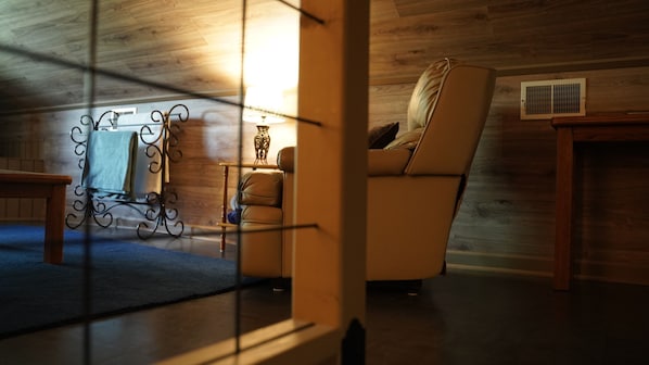 A cozy room with a wooden ceiling, a leather armchair, a small table, and a decorative metal piece. - Lake Escape #2 in Hocking Hills (Logan)