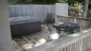 A wooden deck with a hot tub, a round table, and metal chairs.