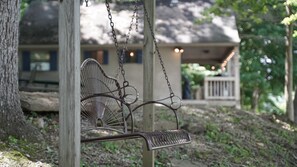Une balançoire en métal suspendue à un poteau en bois, avec une maison en arrière-plan.
