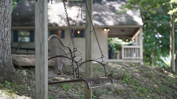 A metal swing chair hanging from a wooden post, with a house in the background.