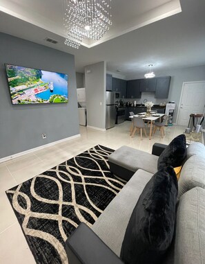 A modern living room with a grey sofa, black and white rug, and a large TV displaying a scenic view.