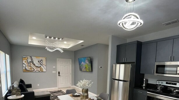 Una cocina moderna con electrodomésticos de acero inoxidable, un comedor con una mesa blanca y sillas grises, y un sofá gris en la sala de estar.