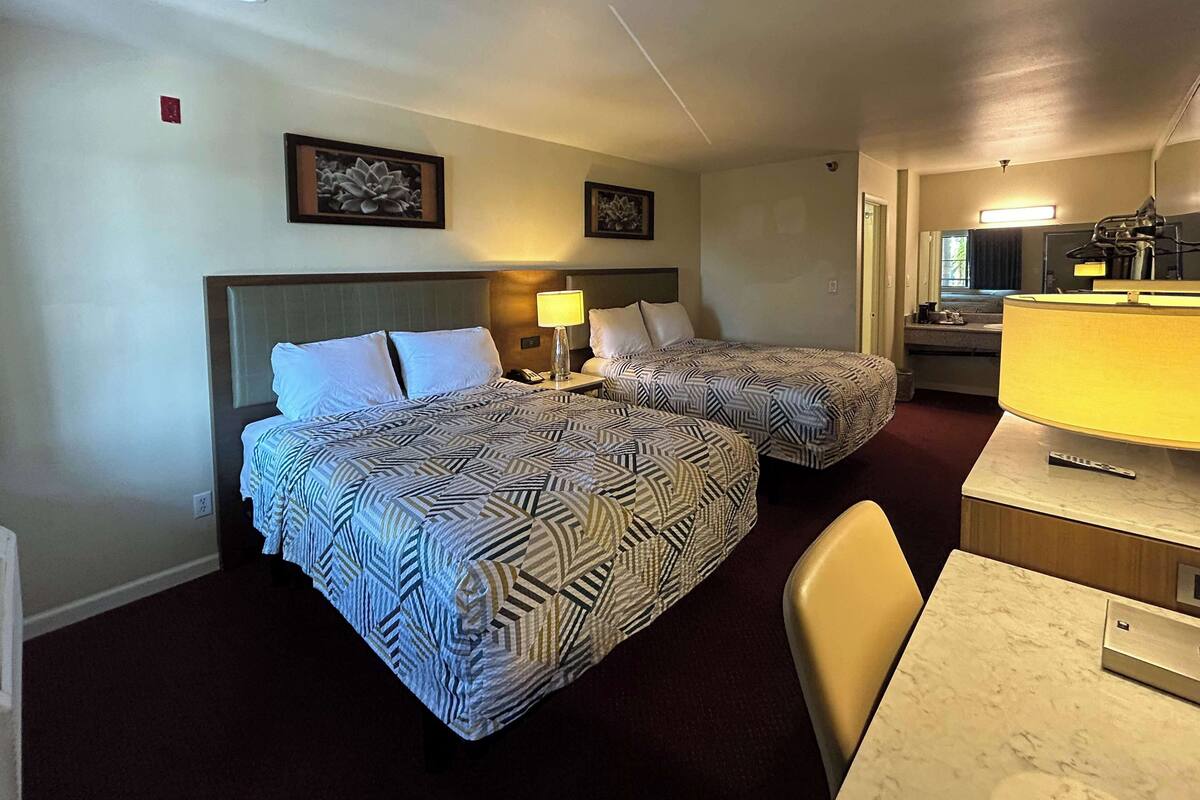 A hotel room with two beds, a desk, a chair, and a bathroom visible through an open door.