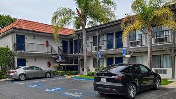 Un edificio de varios pisos con techo de tejas rojas, un estacionamiento con espacios reservados para discapacitados y un Tesla estacionado en un lugar designado.