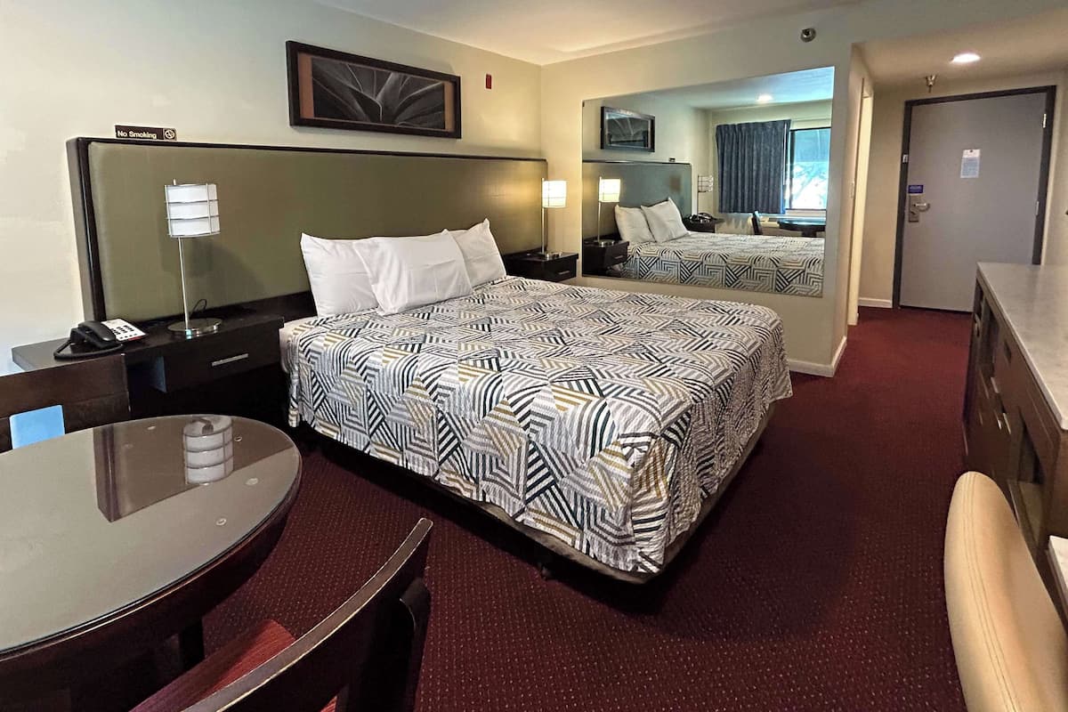 A hotel room with a large bed, a desk, a chair, a mirror, and a door.