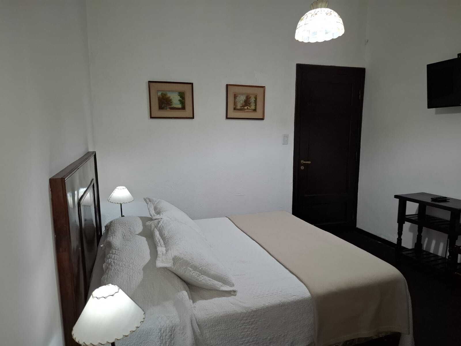 A bedroom with a bed, two wall-mounted pictures, a door, and a small table.