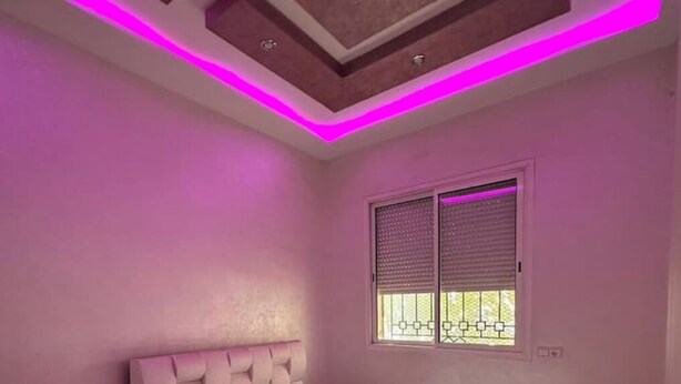 A bedroom with a bed, a window with blinds, and a ceiling with pink lighting. - marrakesh apartment (Marrakech)