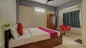 A bedroom with a bed, a ceiling fan, an air conditioning unit, a wooden wardrobe, a small table with chairs, and a window with curtains. - Hotel Light House Comforts - Mysore (Mysore)