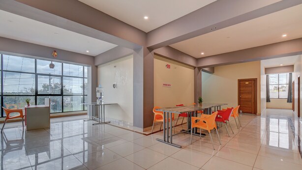 A modern hotel lobby with a large window, a reception desk, a dining area with orange chairs, and a wooden door. - Hotel Light House Comforts - Mysore (Mysore)