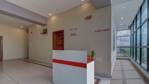 A reception area with a reception desk, a wooden door, and signs indicating reception hours and directions to rooms. - Hotel Light House Comforts - Mysore (Mysore)