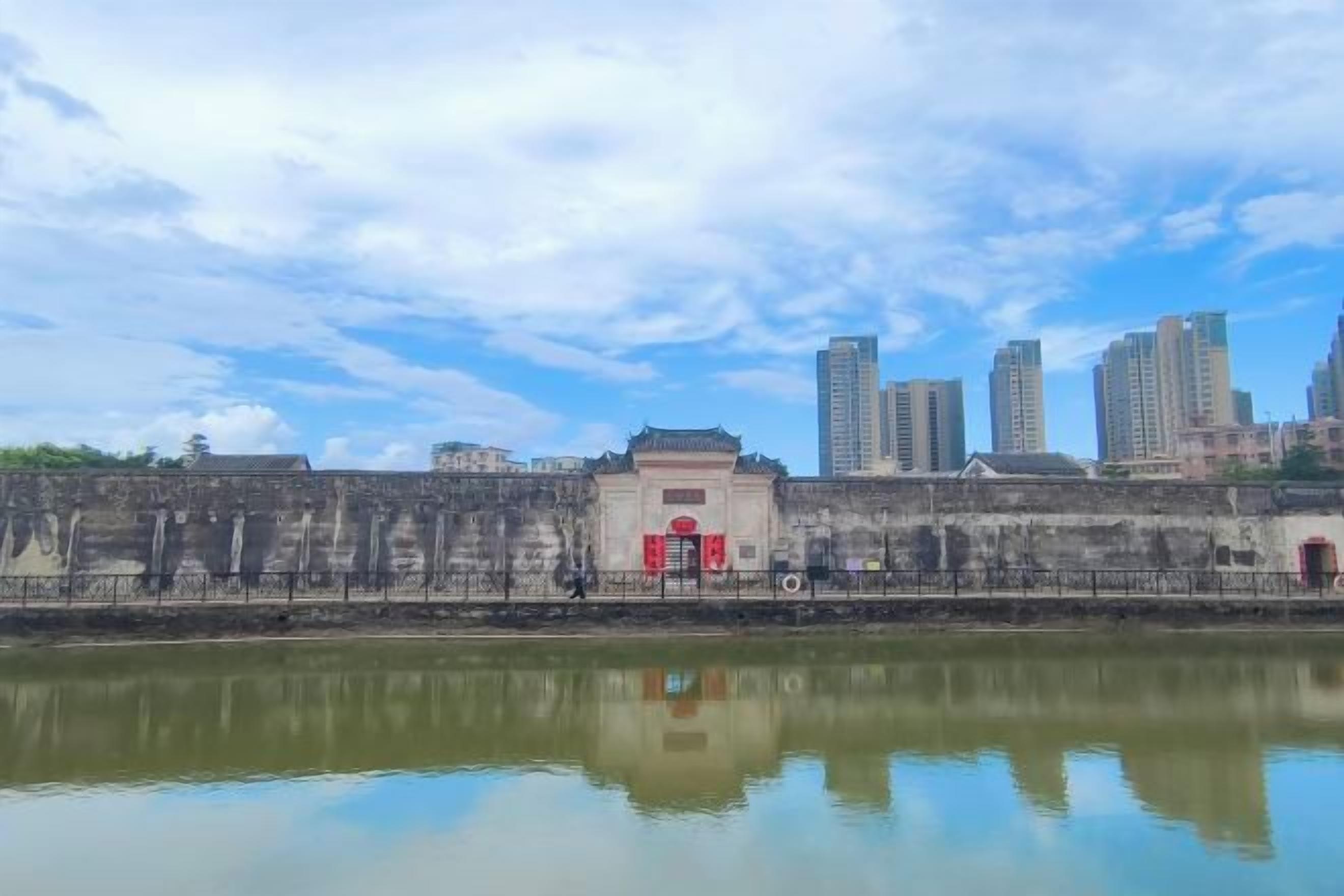 A historic building with a traditional architectural style, a body of water in the foreground, and modern high-rise buildings in the background.