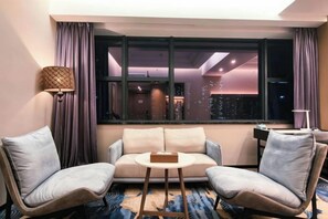 A hotel room with a sofa, two armchairs, a small table, and a window with a city view.