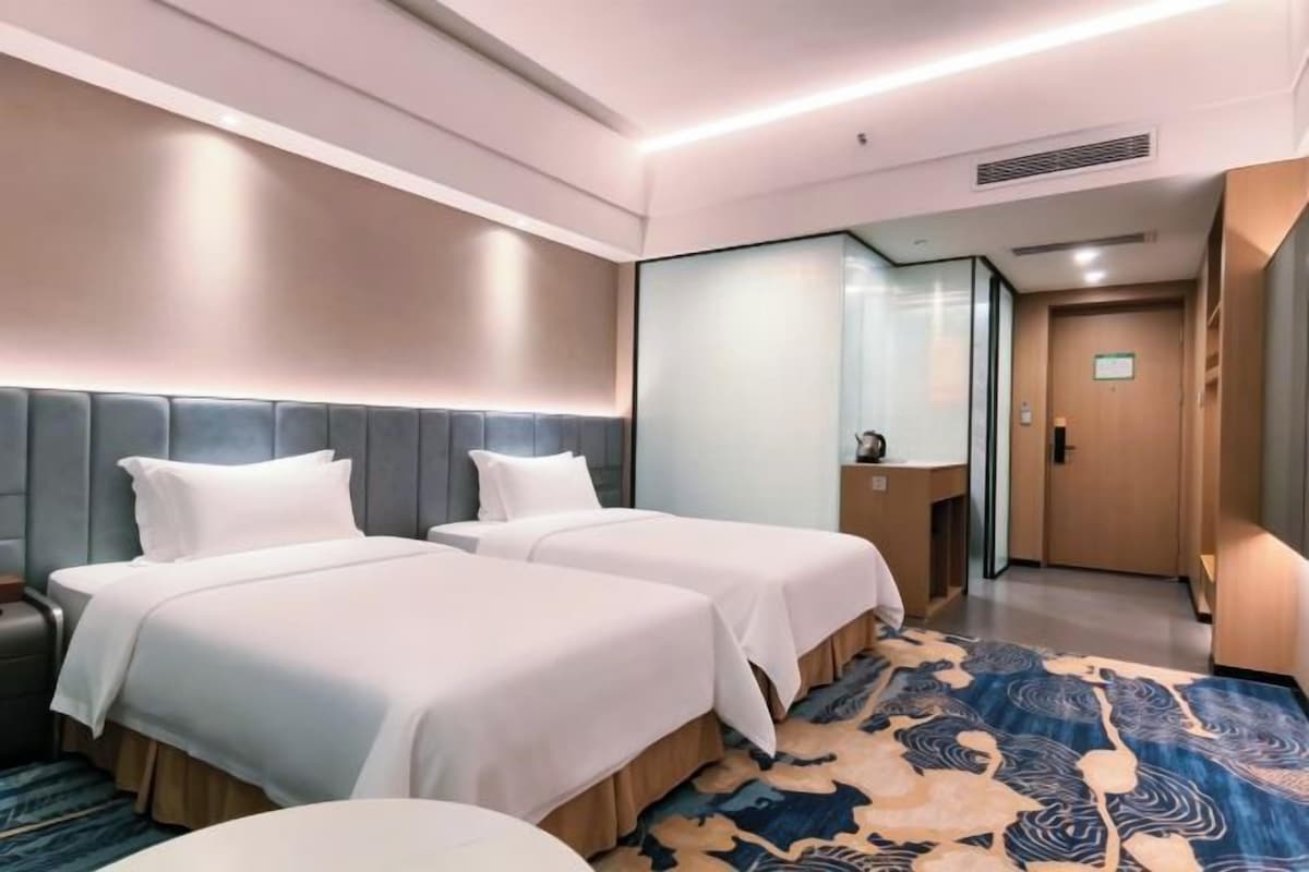 Quarto de hotel com duas camas, um espelho grande, uma escrivaninha e piso coberto de carpete.