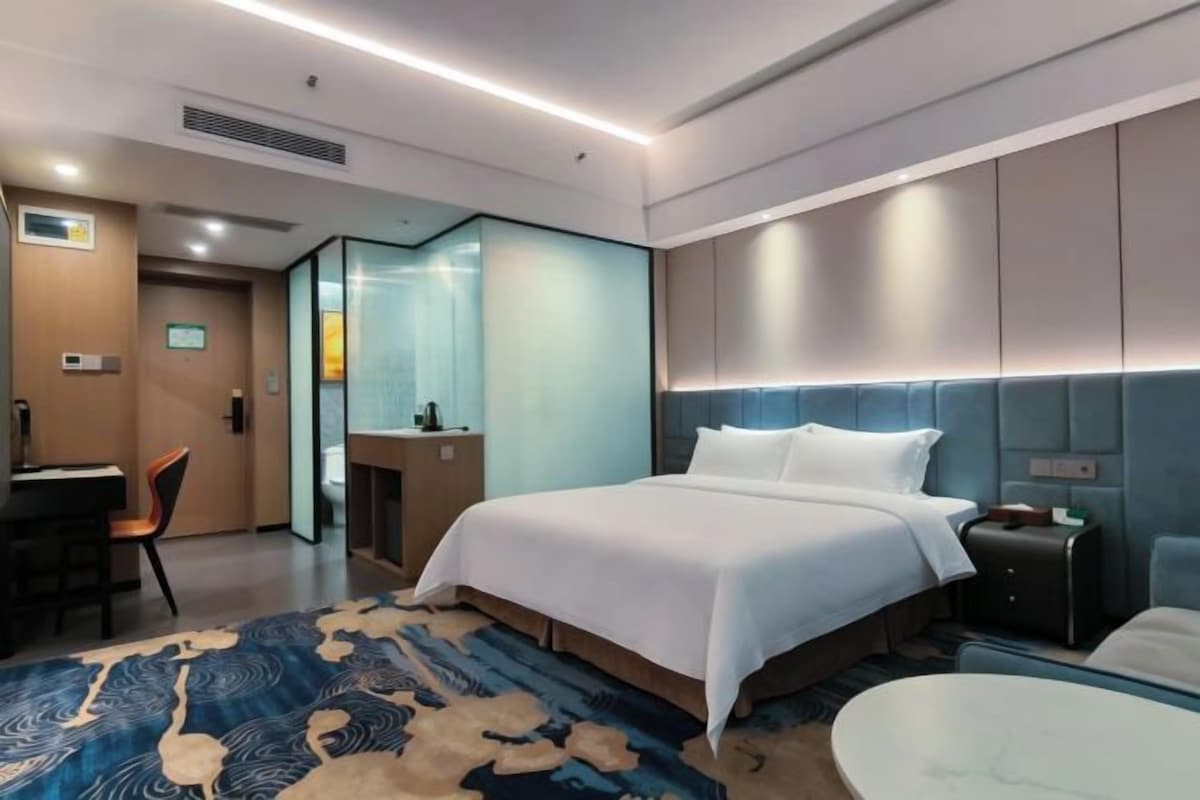 Quarto de hotel com cama, escrivaninha, cadeira, mesa redonda e banheiro.