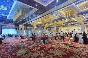 Un salón de banquetes con mesas redondas, una alfombra roja y un techo alto con detalles ornamentales.