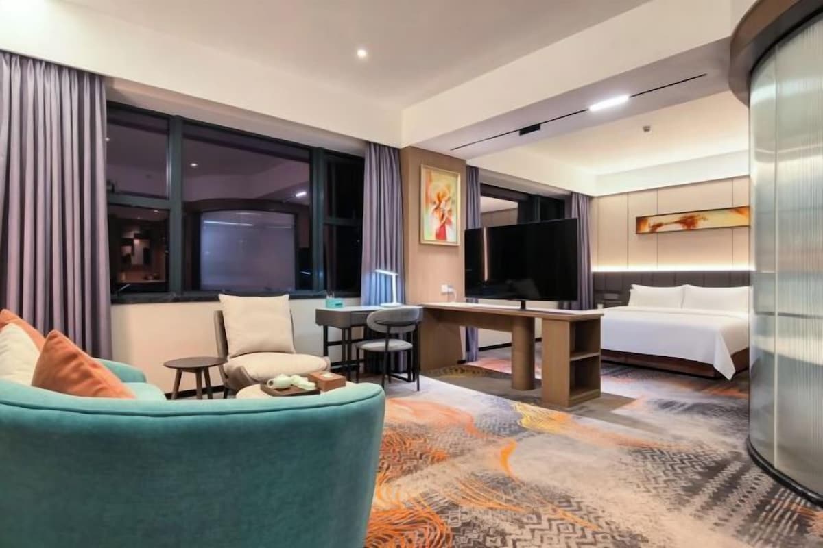 Quarto de hotel com sofá, escrivaninha, cama e televisão.