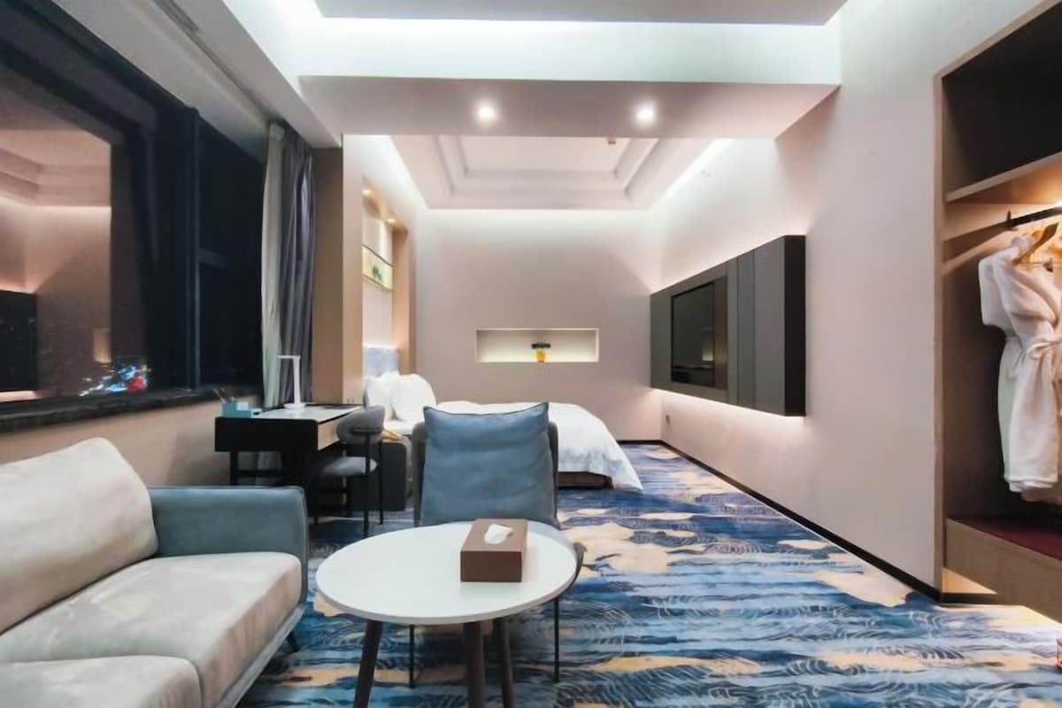 Quarto de hotel com sofá, mesa redonda, cama, escrivaninha e televisão.