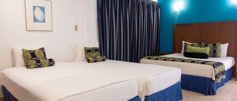 A hotel room with two beds, a large window with curtains, a wooden ceiling, and a framed picture on the wall.