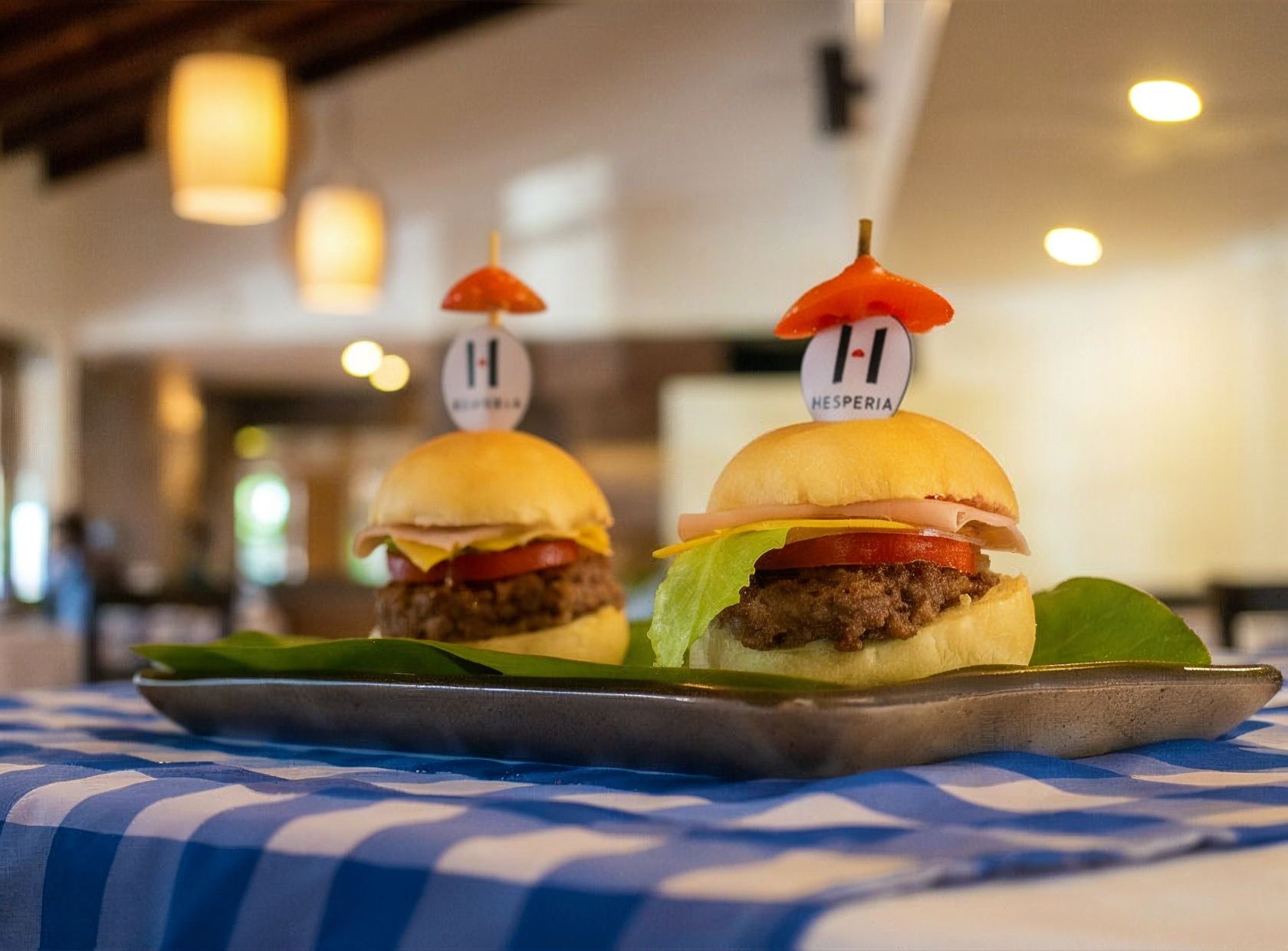 Dos hamburguesas en una bandeja con mantel a cuadros, cada una con un adorno con forma de bandera.