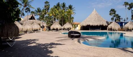 A pool area with thatched umbrellas, palm trees, and lounge chairs.
