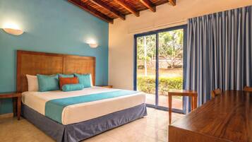Habitación de hotel con cama, cabecera de madera, mesa de comedor y vista a través de un ventanal.
