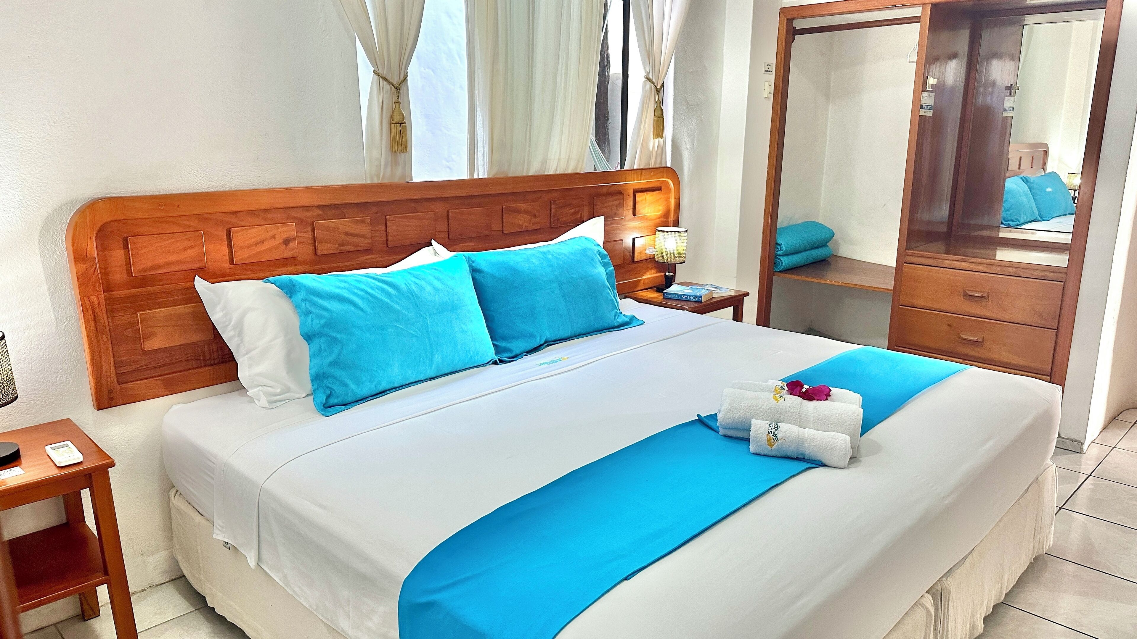 A neatly made bed with blue and white bedding, a wooden headboard, a bedside table with a lamp, and a mirror on the wall.