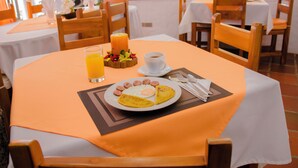 A breakfast table set with a plate of eggs, sausages, and toast, a glass of orange juice, and a candle. - Hostal Suenos Silvestres (Puerto Ayora)