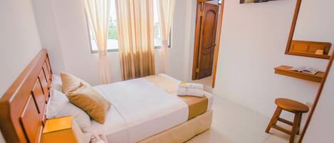A hotel room with a bed, a bedside table with a lamp, a TV mounted on the wall, and a window with curtains.