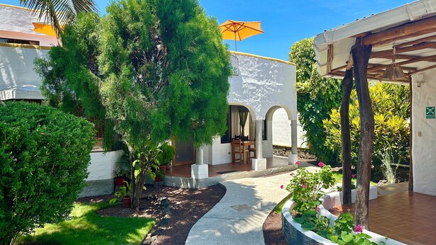 A courtyard with a covered seating area, a pergola, and a sign indicating a meeting point. - Hostal Suenos Silvestres (Puerto Ayora)