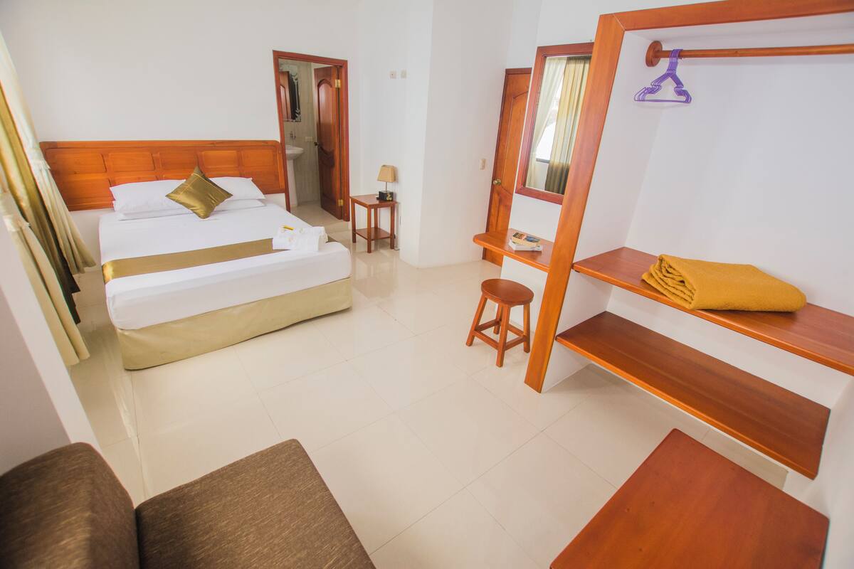 Une chambre d’hôtel avec un lit, un bureau, une chaise, un miroir et une étagère en bois.