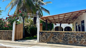 A stone-walled building with a wooden gate, a covered patio, and a view of a mountain range. - Hostal Suenos Silvestres (Puerto Ayora)