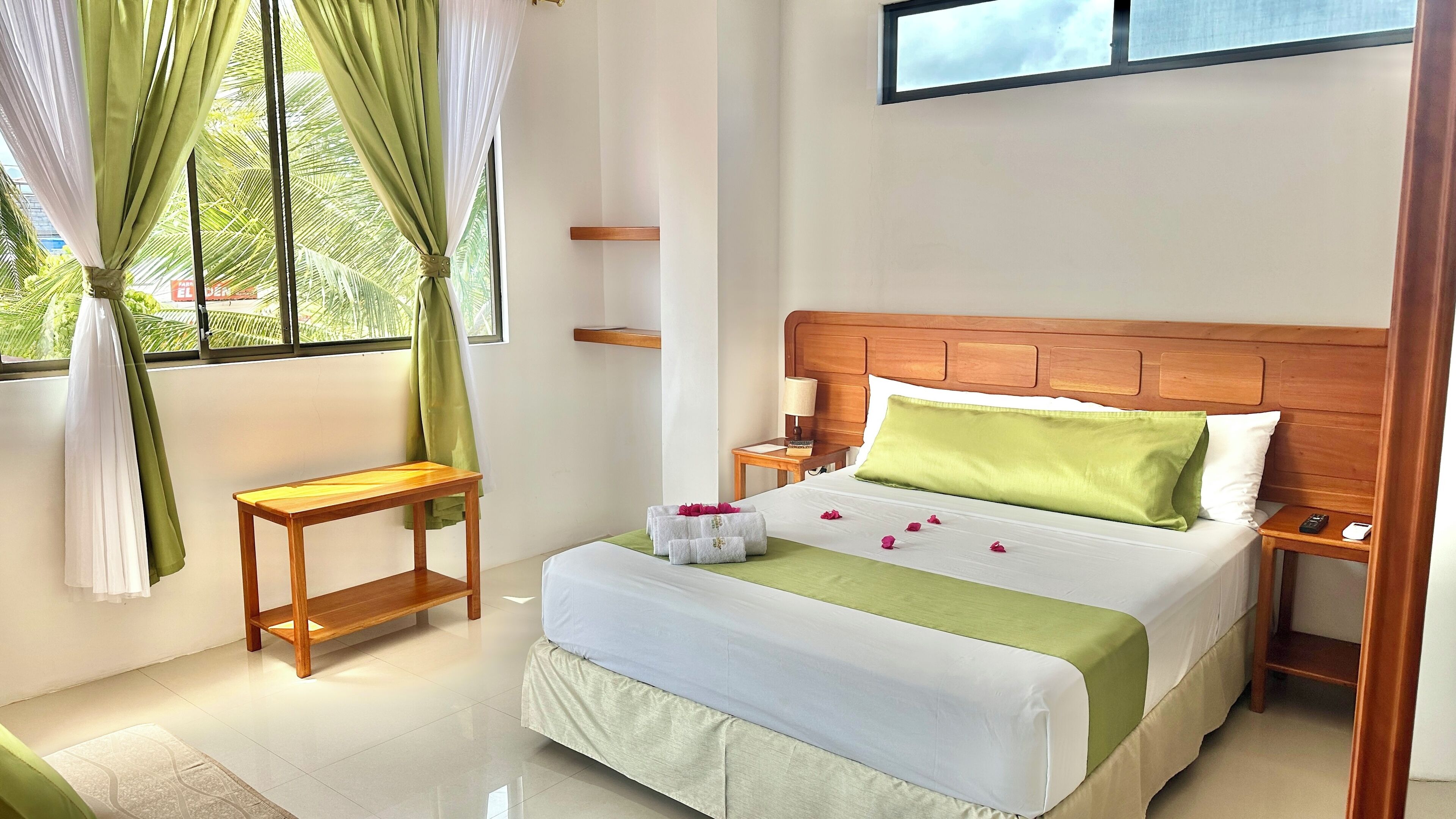 Une chambre d’hôtel bien rangée, avec un lit, des tables de chevet, une petite table et une fenêtre avec des rideaux.
