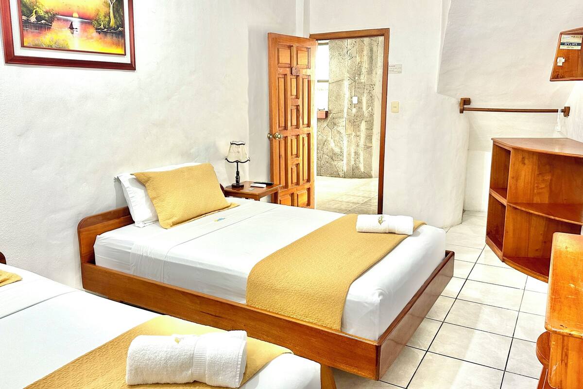 Une chambre d’hôtel avec un lit en bois, une table de chevet avec une lampe, une armoire en bois et un tableau encadré au mur.