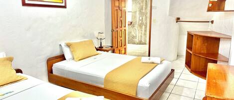 A hotel room with a wooden bed, a bedside table with a lamp, a wooden wardrobe, and a framed picture on the wall.
