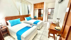 A hotel room with two beds, a wooden headboard, a small desk with a lamp, and a mirror. - Hostal Suenos Silvestres (Puerto Ayora)
