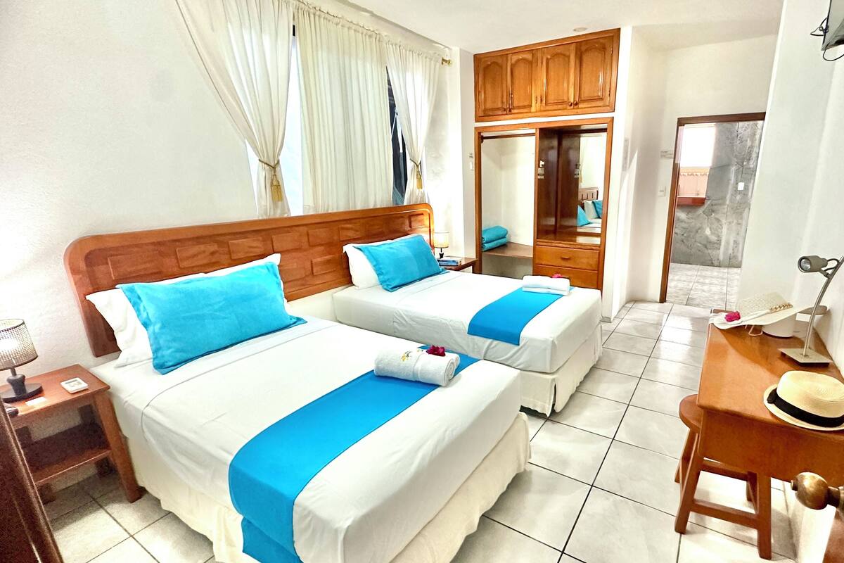 Une chambre d’hôtel avec deux lits, une tête de lit en bois, un petit bureau avec une lampe et un miroir.