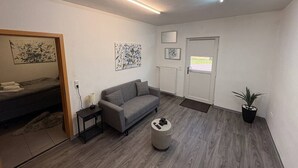 A modern living room with a grey sofa, a small round table, a potted plant, and artwork on the walls. - Studio One - 5 min to Grafenwöhr (Pressath)