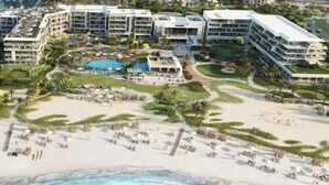 A resort with multiple buildings, a central pool, and a beach area with sun loungers.