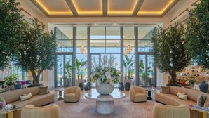 A spacious lobby with a central coffee table surrounded by sofas, large windows, and indoor plants.