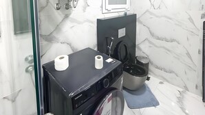 Pieni kylpyhuone, jossa on pyykinpesukone, wc ja suihkutila.