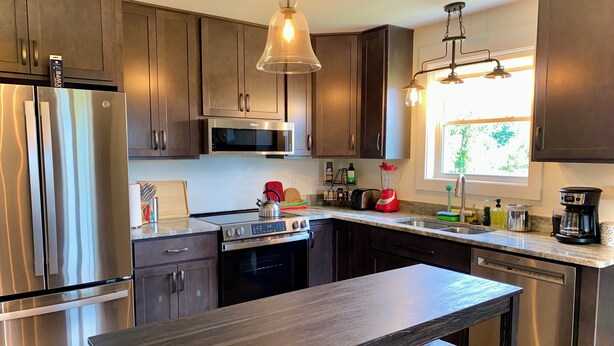 Cocina moderna con electrodomésticos de acero inoxidable, armarios de madera oscura, una isla central con asientos e iluminación colgante.