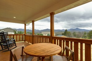 A wooden deck with a round table and chairs, overlooking a mountainous landscape. - Modern Shepherd's Lodge with stunning 360 Views, Fenced Pet Area and Pool (Buncombe County)